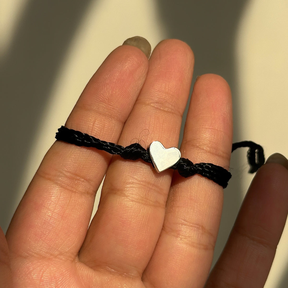 little heart thread band – 925 sterling silver heart charm on an adjustable black braided cord, held across a hand